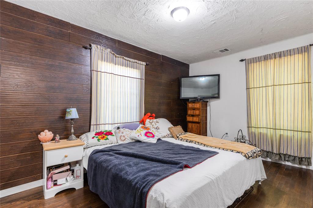 548 Elston Drive Dallas, TX 75232 - Photo 9 of 18 Bedroom featuring wood walls, a textured ceiling, and dark wood-style floors