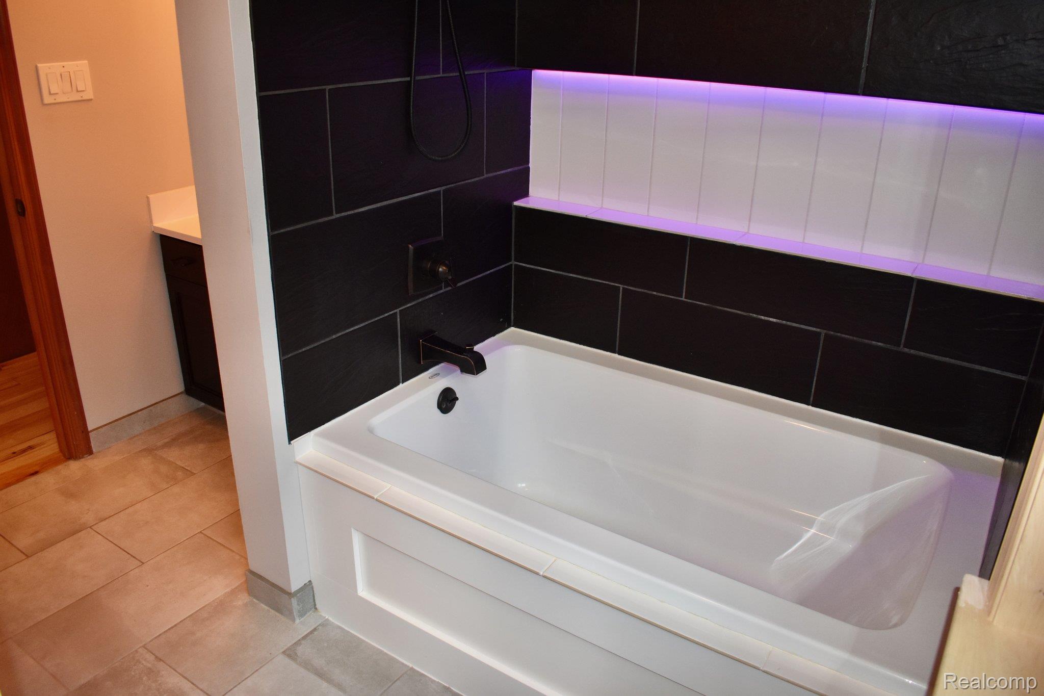 8312 Whitmore Lake Road Brighton, MI 48116 - Photo 36 of 43 Built-in bathtub with dark tile surround, integrated shower niche with accent lighting, and matte black fixtures