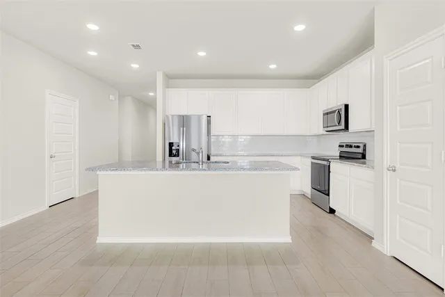 a large white kitchen with kitchen island a sink a refrigerator and white cabinets