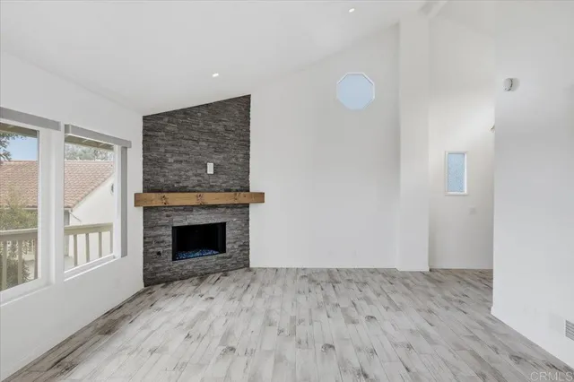 a view of an empty room with wooden floor fireplace and a window