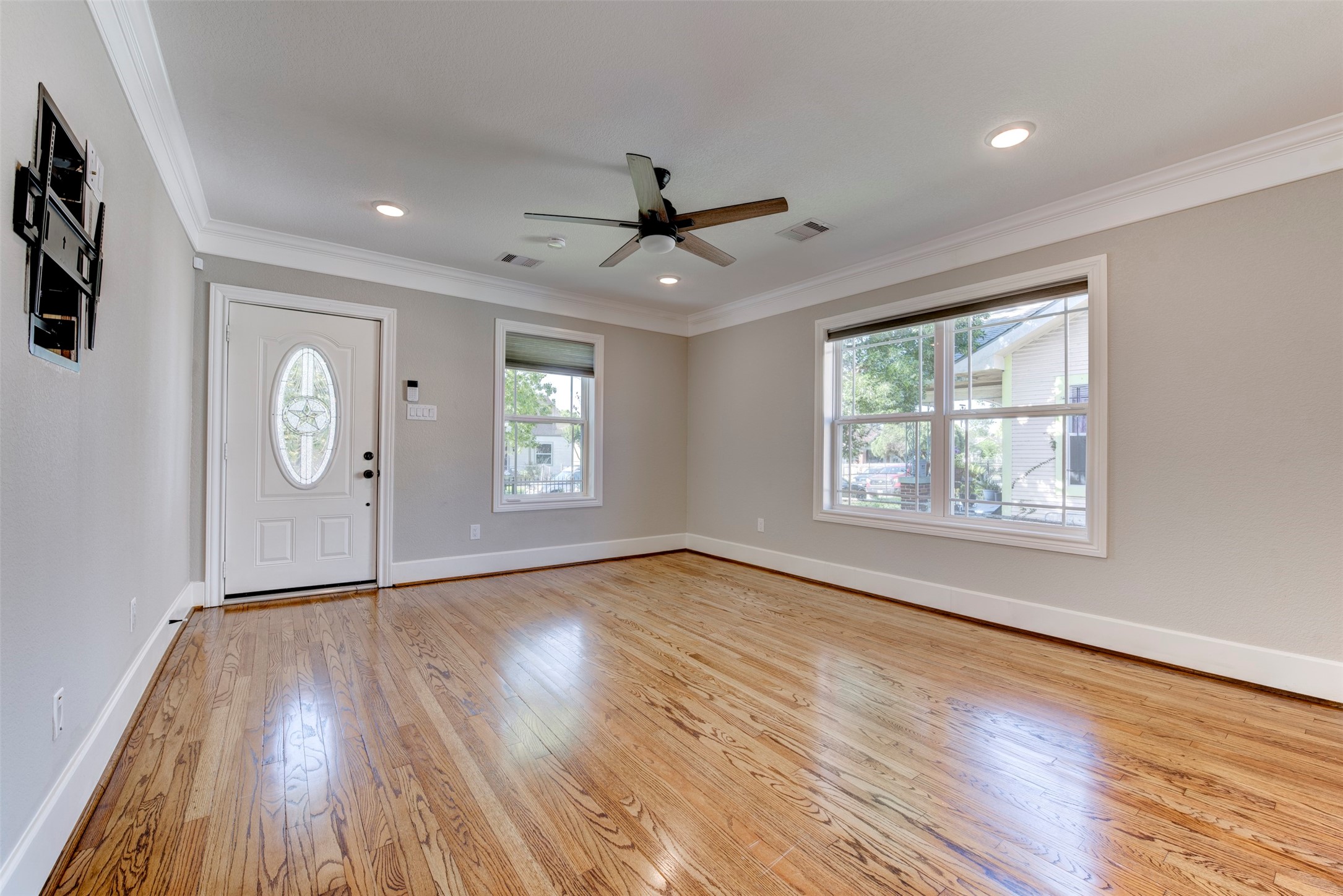 109 Dresden Street Houston, TX 77012 - Photo 9 of 43 Bright and airy living room with polished hardwood floors, recessed lighting, and a ceiling fan. Features large windows for natural light and a stylish front door with decorative glass.