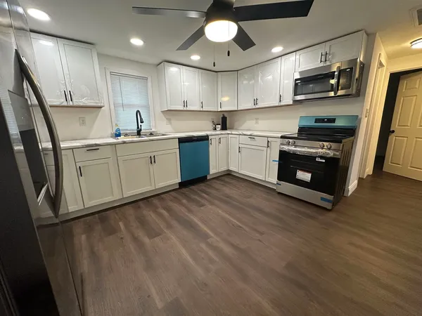 a kitchen with stainless steel appliances granite countertop a refrigerator a oven a sink dishwasher and white cabinets with wooden floor