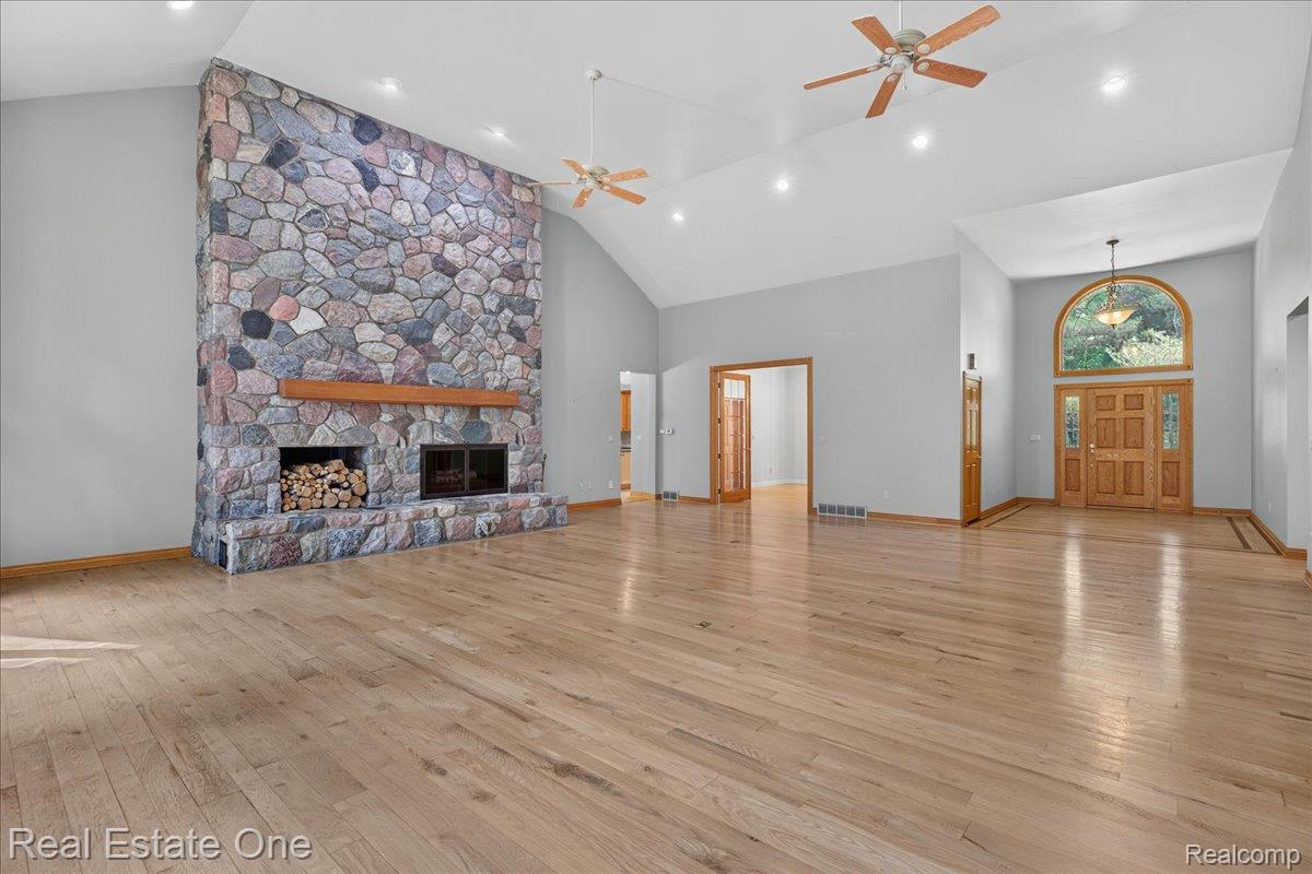 425 Courtney Road Leonard, MI 48367 - Photo 11 of 89 Spacious interior featuring a floor-to-ceiling stone fireplace with a wood mantle, vaulted ceilings, recessed lighting, and wood-finish flooring