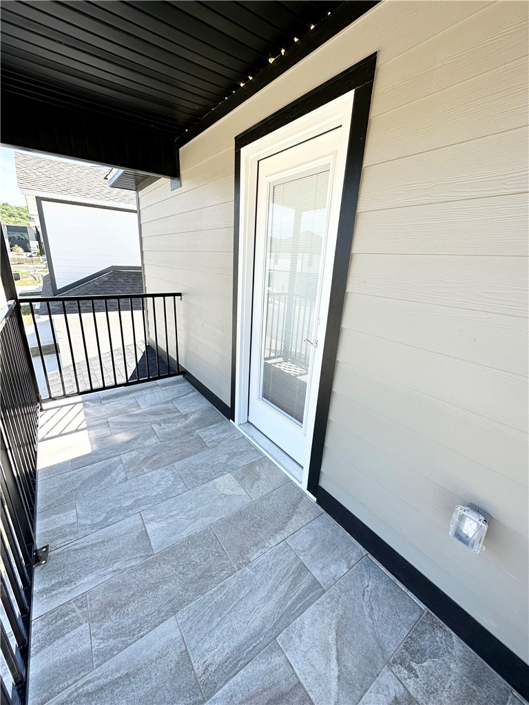 The property features a balcony with textured gray tile flooring, a black metal railing, and a full-light glass door