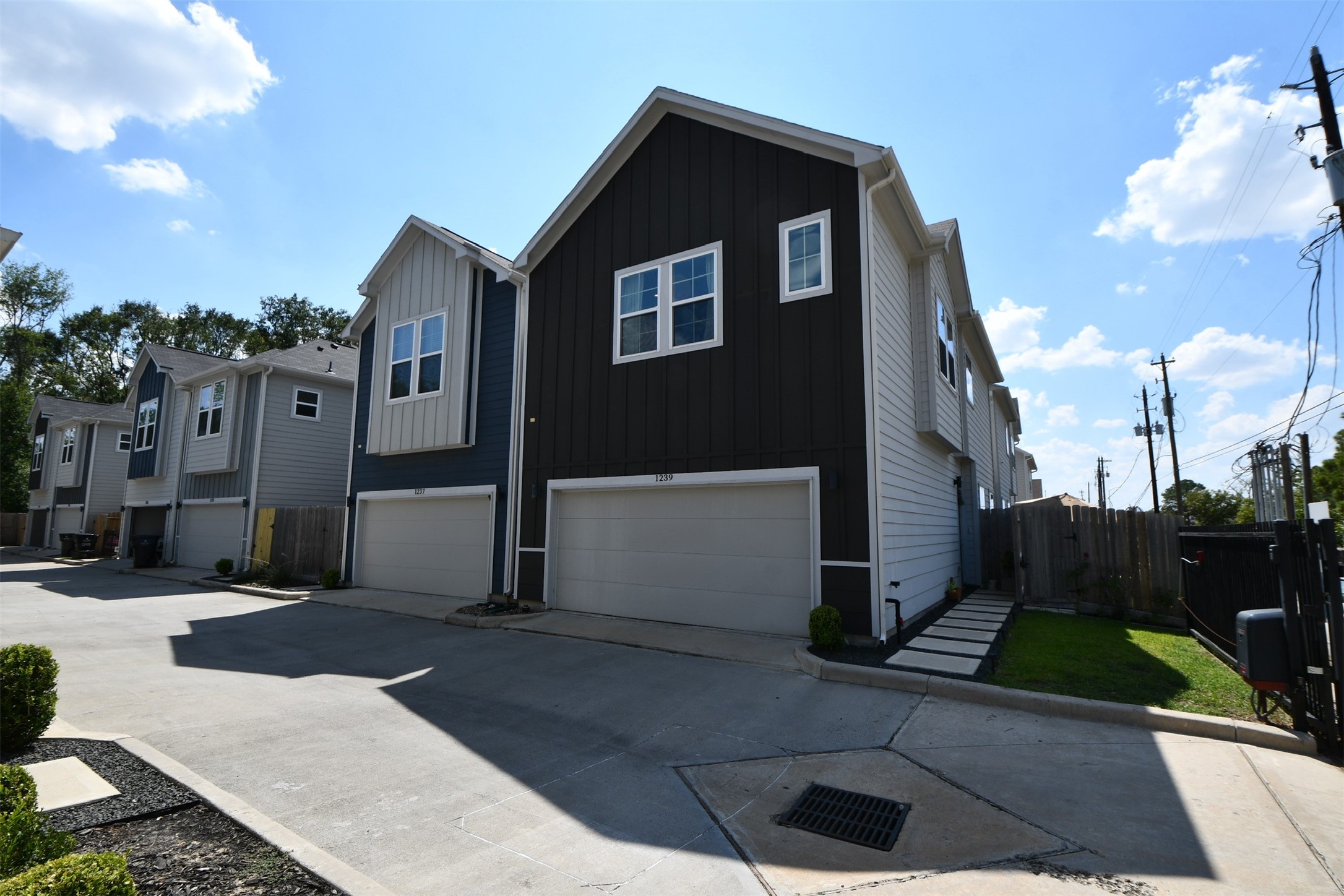 Modern townhouses with a gated entrance provide security and privacy. The exterior features a mix of light and dark siding, with a private driveway leading to multiple units. A "No Parking" sign is visible, indicating controlled access.