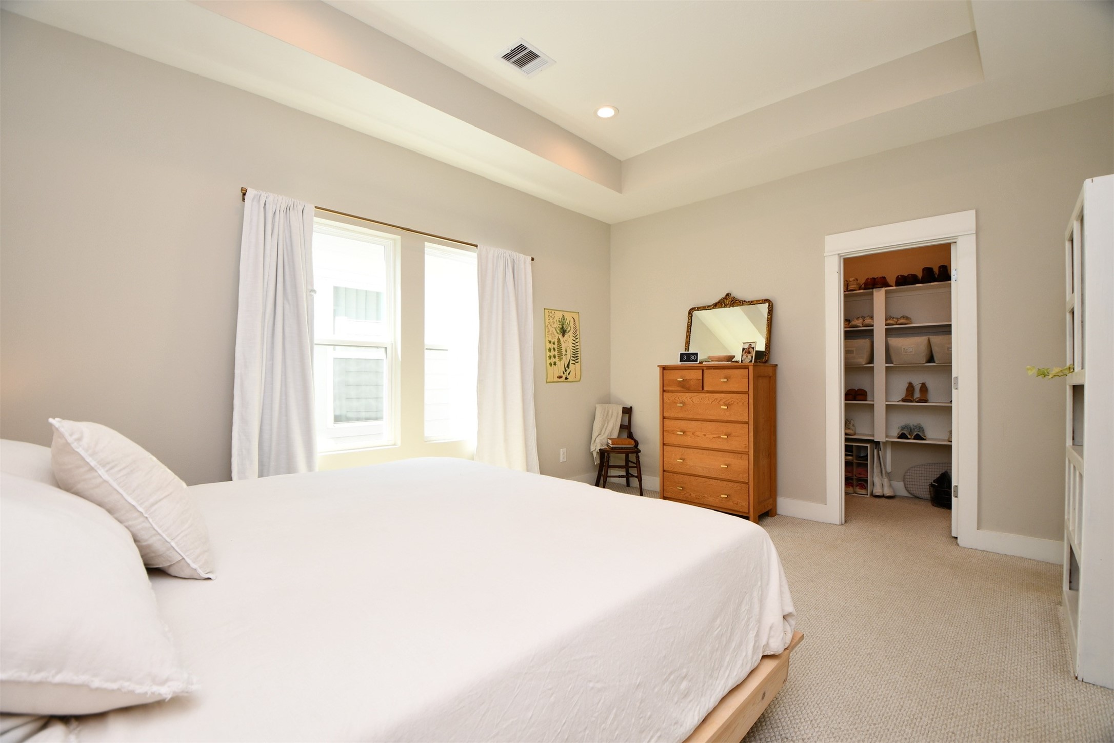 1239 West Tidwell Road Houston, TX 77091 - Photo 19 of 35 This photo showcases a bright, spacious bedroom with a large window allowing natural light. It features a comfortable bed, a wooden dresser with a mirror, and an open closet with ample shelving. The neutral color palette and recessed ceiling add a modern touch.