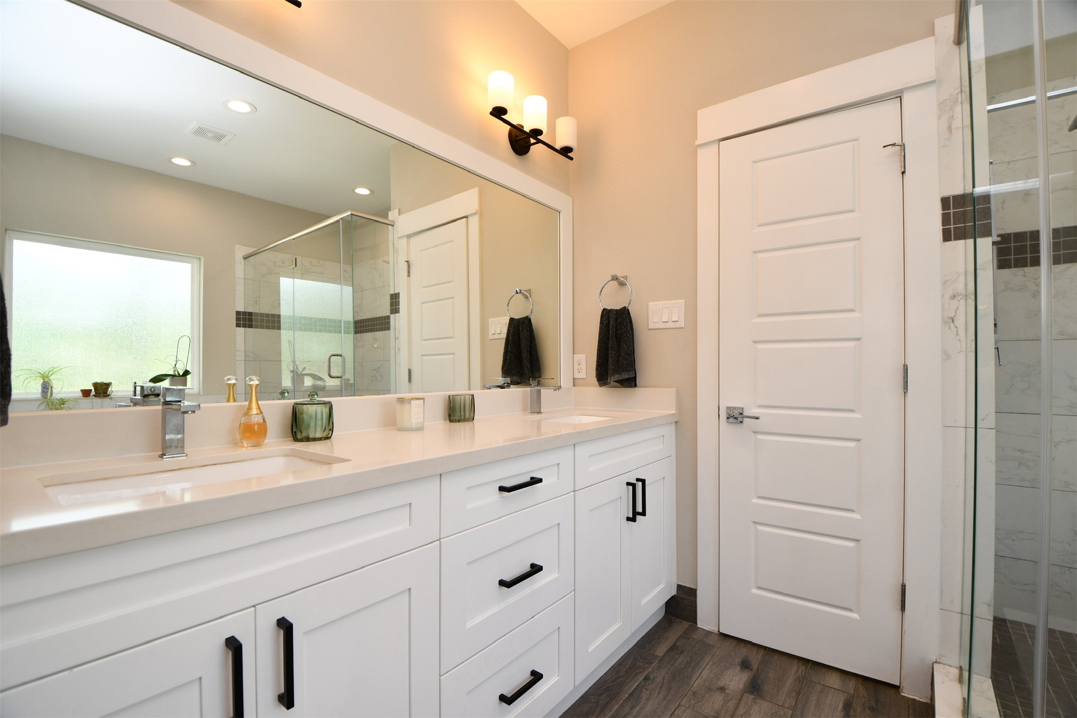 1239 West Tidwell Road Houston, TX 77091 - Photo 22 of 35 This modern bathroom features a large double vanity with sleek white cabinetry and black hardware. It includes a spacious frameless glass shower, ample lighting, and a neutral color palette, creating a bright and inviting space.