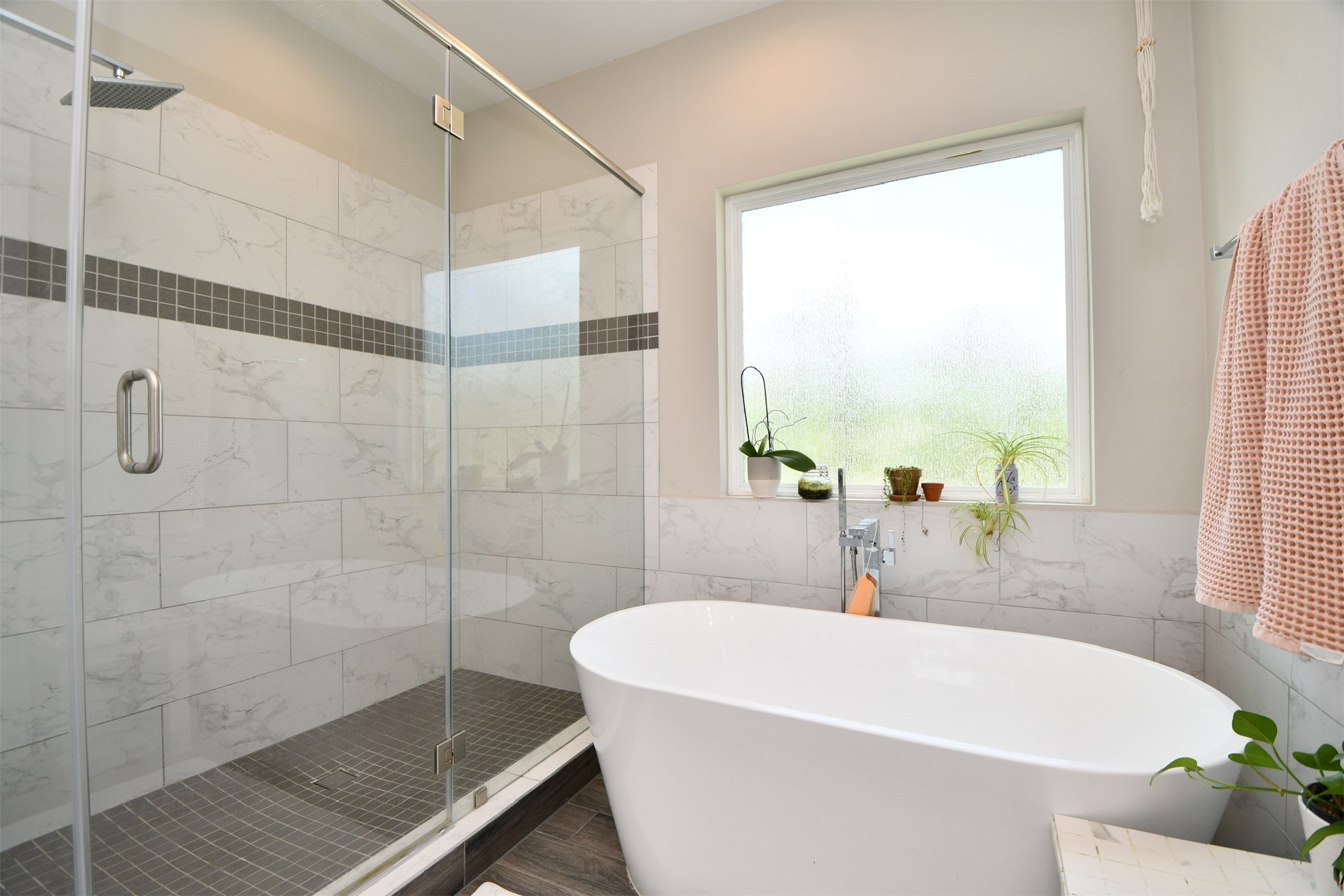 1239 West Tidwell Road Houston, TX 77091 - Photo 24 of 35 This bathroom features a modern design with a spacious glass-enclosed shower, elegant tile work, and a freestanding bathtub. Natural light fills the room through a large frosted window, creating a serene atmosphere.