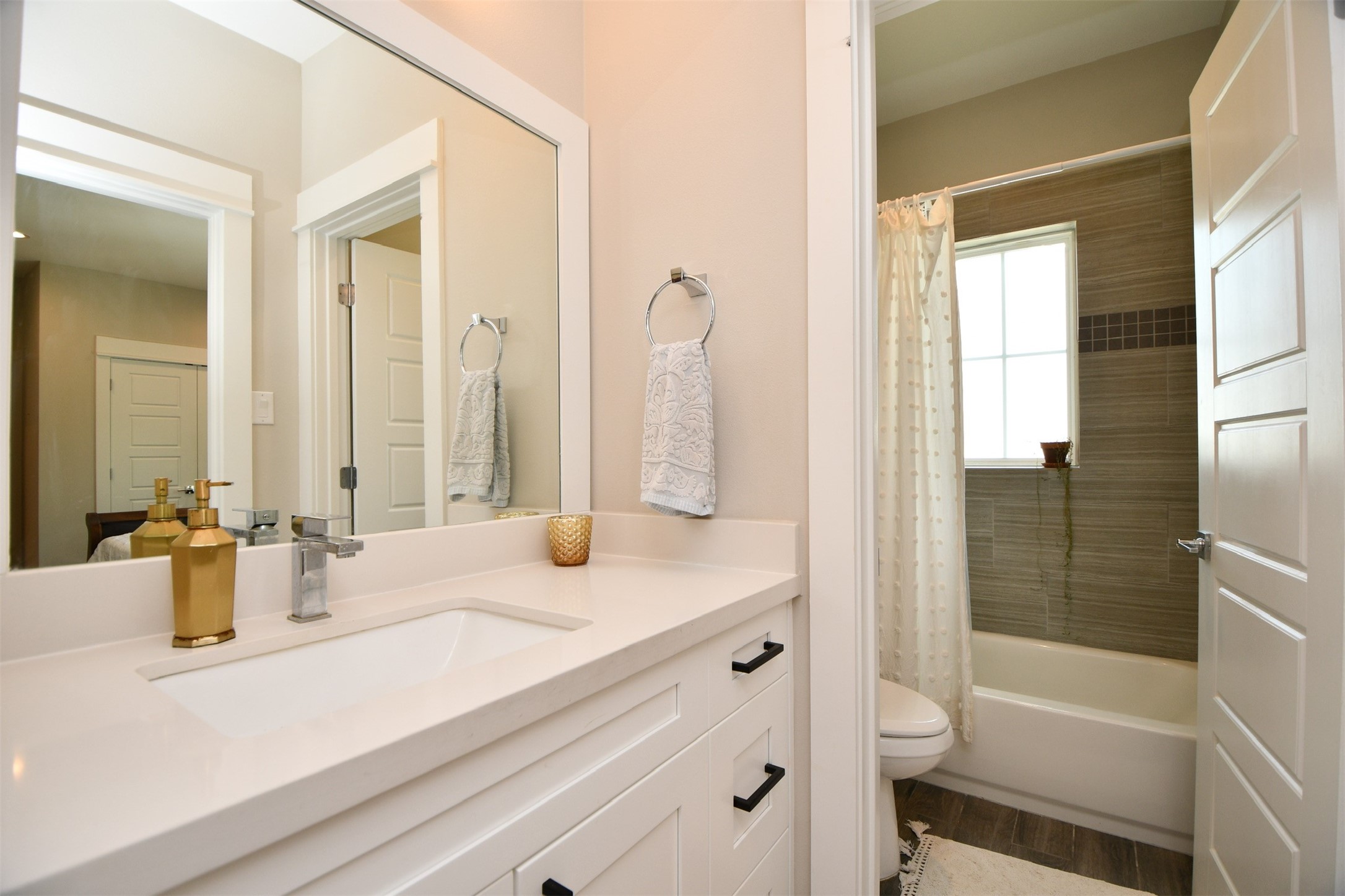 1239 West Tidwell Road Houston, TX 77091 - Photo 28 of 35 This bathroom features a modern design with a sleek white vanity and ample storage. It includes a bathtub with a tiled shower area, a large mirror, and contemporary fixtures, providing a clean and inviting space.