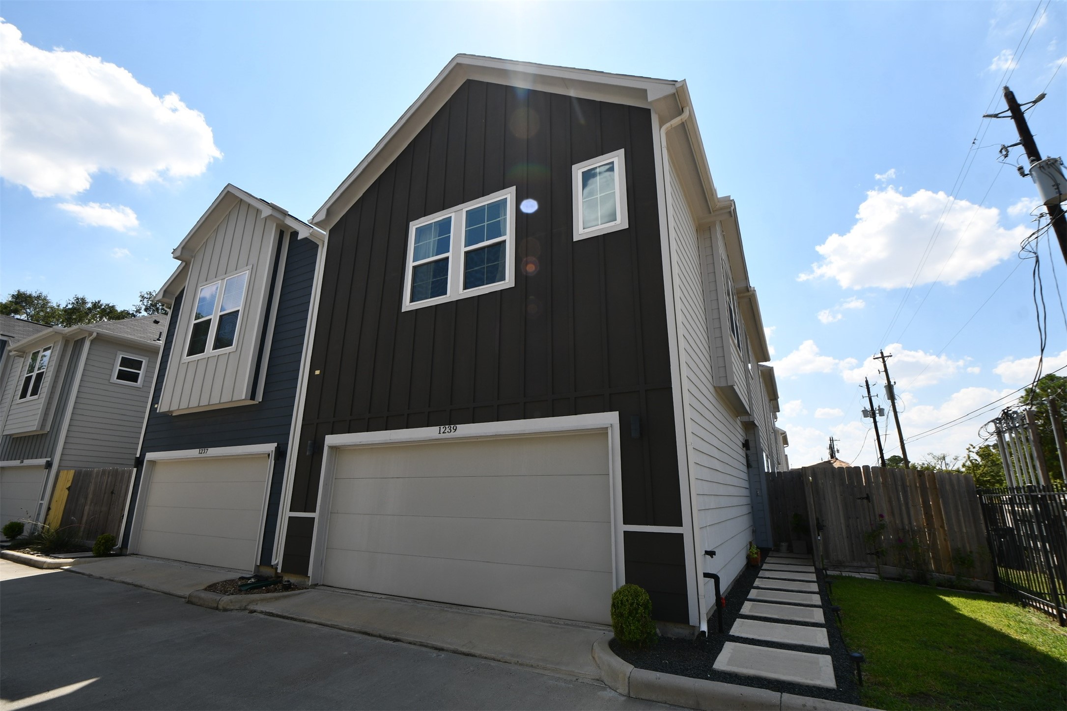 1239 West Tidwell Road Houston, TX 77091 - Photo 3 of 35 This photo shows a modern, two-story home with a dark exterior and a white trim. It features a double garage and multiple windows for natural light. The house is situated in a residential neighborhood with nearby trees and a fenced area.