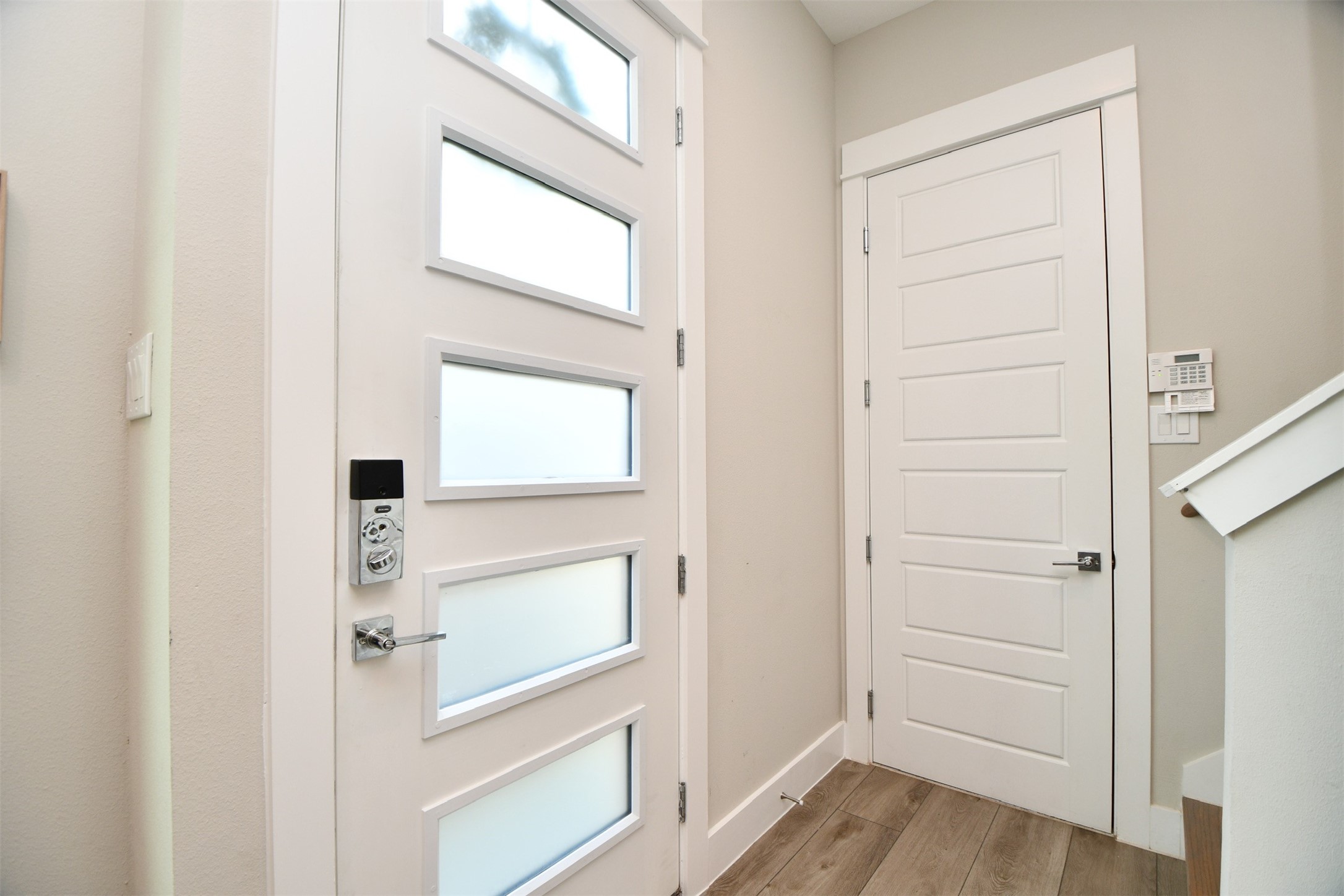 1239 West Tidwell Road Houston, TX 77091 - Photo 5 of 35 This photo shows a modern entryway featuring a stylish door with frosted glass panels, light-colored walls, and wood flooring. There’s a security keypad next to the interior door, indicating a secure and welcoming entrance.