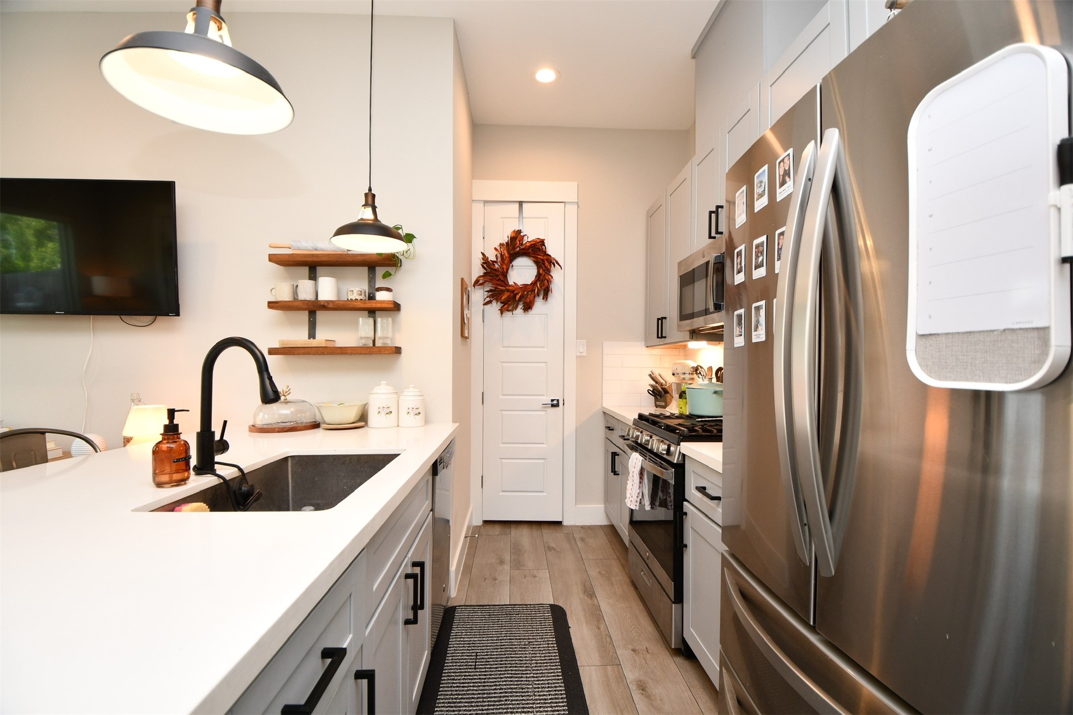 1239 West Tidwell Road Houston, TX 77091 - Photo 8 of 35 Modern kitchen with sleek stainless steel appliances, white cabinetry, and a stylish black faucet. The open layout includes a large island with pendant lighting, a wall-mounted TV, and decorative shelving. The space is cozy and well-lit, ideal for cooking and entertaining.