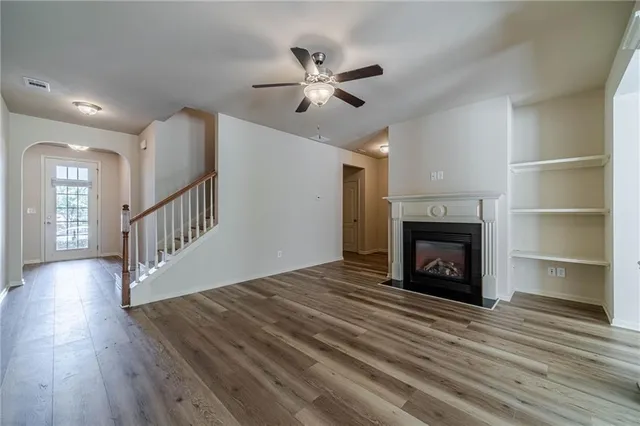 a view of an empty room with wooden floor and a ceiling fan