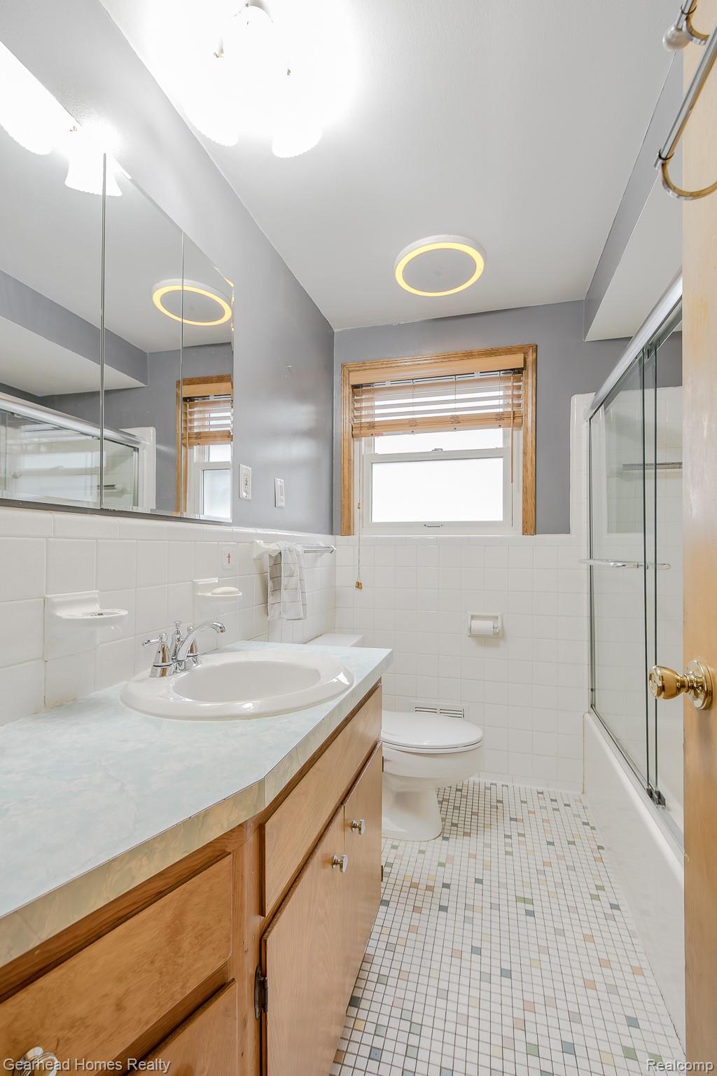 3356 Harding Street Dearborn, MI 48124 - Photo 18 of 48 Vanity with a built-in sink, wall-mounted mirror, white tile walls, a window with wood trim, and mosaic floor tiling