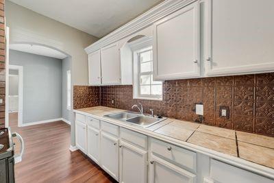 930 Freeman Street Sherman, TX 75092 - Photo 8 of 18 Kitchen featuring white cabinetry, a double basin stainless steel sink, a tiled countertop, and a decorative brown backsplash