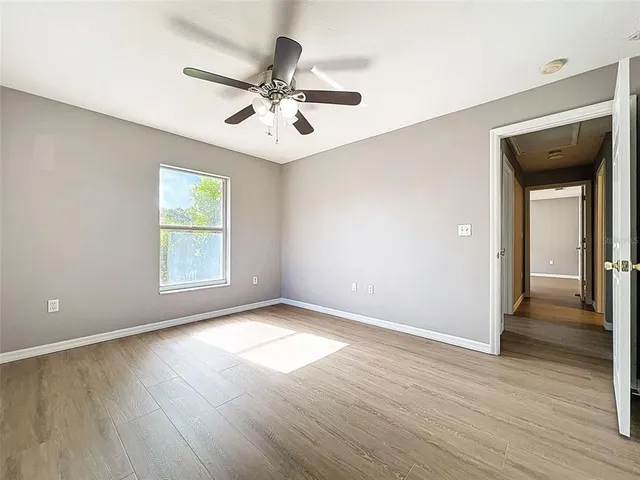 an empty room with wooden floor chandelier fan and windows
