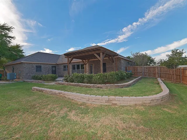 a view of a white house in front of a big yard with plants and large trees