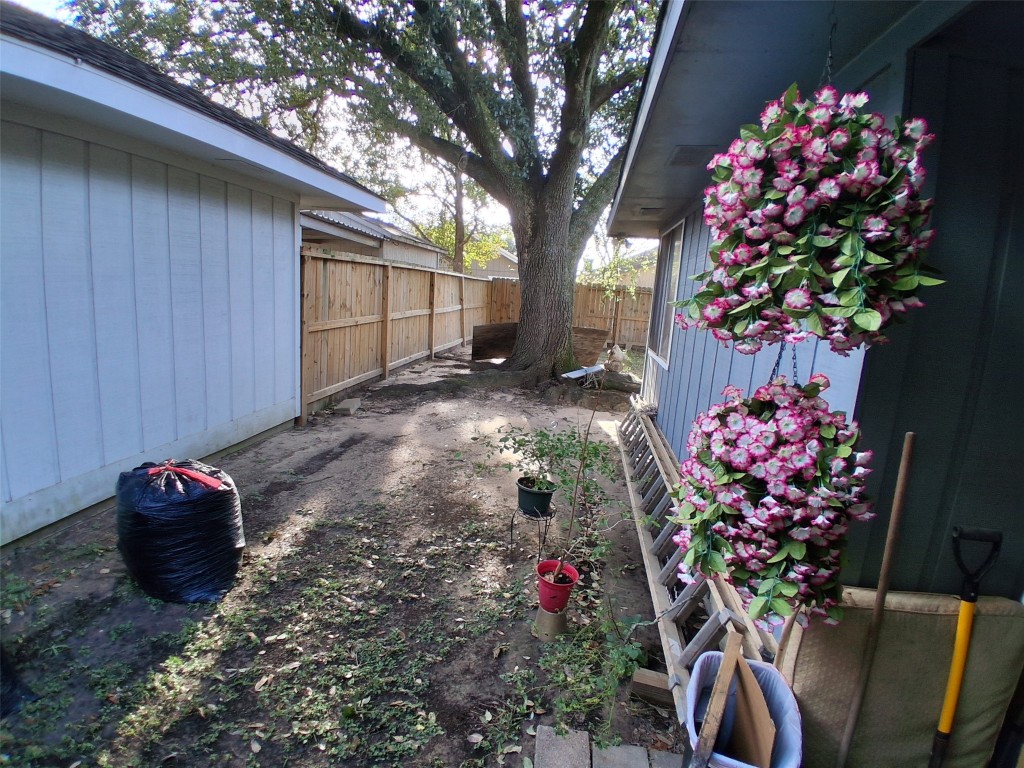 23347 Pebworth Place Spring, TX 77373 - Photo 9 of 10 This charming side yard offers a serene space with vibrant hanging flowers and a majestic tree, perfect for gardening or relaxation.