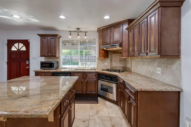 a kitchen with stainless steel appliances granite countertop wooden cabinets a stove top oven a sink and dishwasher