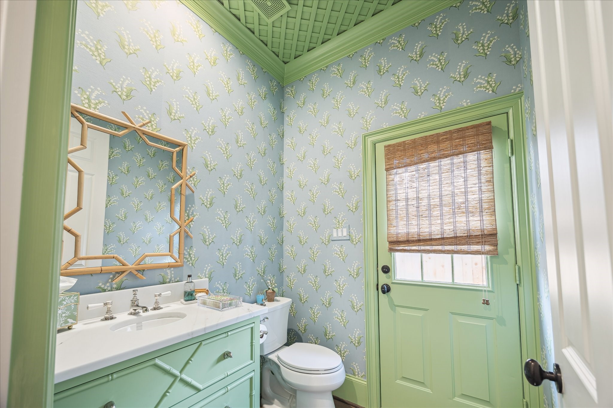 11524 Taylorcrest Road Houston, TX 77024 - Photo 25 of 47 A charming pool bath features Lily of the Valley wallpaper, a lacquered lattice ceiling, and a Waterworks sink with a nickel faucet set in a honed marble custom vanity. Rocky Mountain Hardware finch knobs add a thoughtful detail, while custom “Lucky” green paint by Segreto gives the space a cheerful personality.