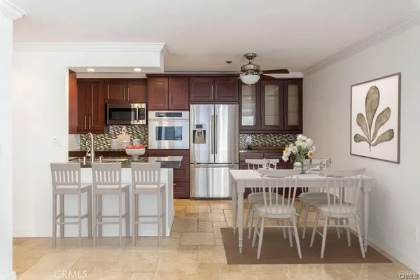 a kitchen with stainless steel appliances kitchen island granite countertop a dining table chairs refrigerator and sink