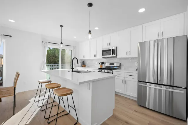 a kitchen with stainless steel appliances a refrigerator a stove a sink dishwasher a dining table and chairs with wooden floor