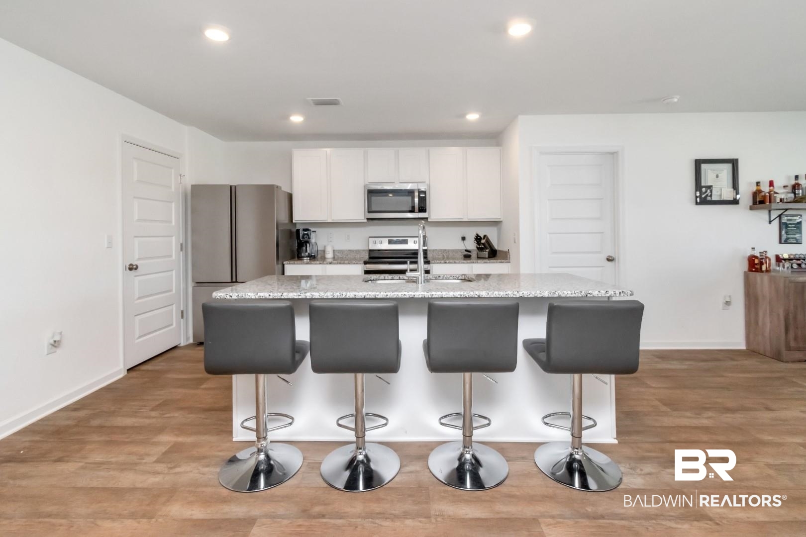 10921 Northern Dancer Court Daphne, AL 36526 - Photo 13 of 32 Kitchen with light stone countertops, stainless steel appliances, white cabinets, light hardwood / wood-style flooring, and a kitchen island with sink