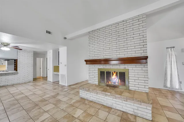 a view of an empty room with a fireplace and a ceiling fan