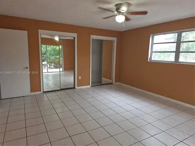 an empty room with chandelier fan and windows