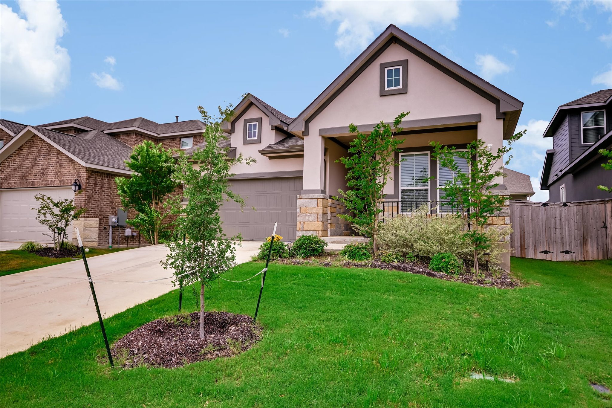 205 Wingstem Way Georgetown, TX 78633 - Photo 2 of 29 Modern facade featuring light-colored stucco, stone accents, and landscaped front yard with young trees.