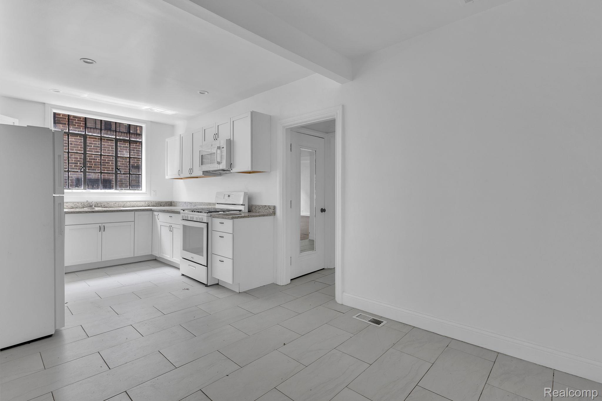 19510 Stratford Road Detroit, MI 48221 - Photo 18 of 45 Kitchen featuring white cabinetry, stone countertops, stainless steel microwave, gas range, and large format tile flooring