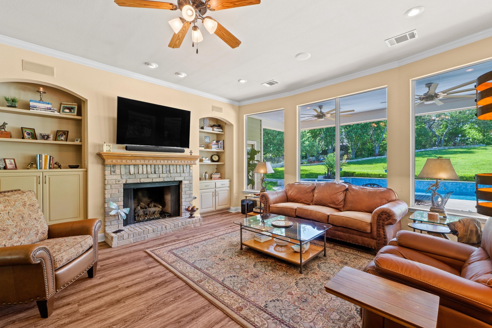 135 Tumbleweed Trail North Austin, TX 78733 - Photo 5 of 39 Living room with built-in shelves, light wood-style floors, ornamental molding, a ceiling fan, and a fireplace that burns real wood or gas logs.