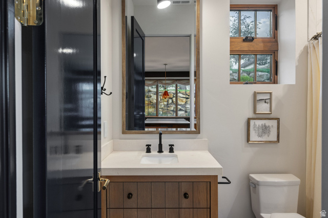 558 West Rheinfalls Circle Midway, UT 84049 - Photo 41 of 61 Contemporary bathroom featuring a wood-finish vanity with dual-handle matte black faucet and white countertop, framed mirror with integrated lighting, black-framed glass shower enclosure, and white porcelain toilet