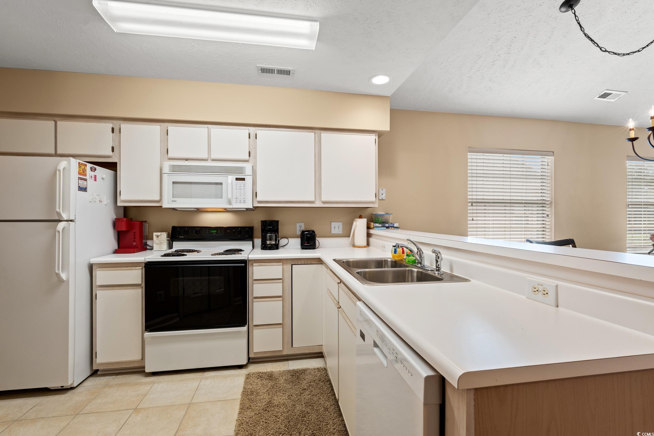 117 Pinehurst Lane, Unit 5E Pawleys Island, SC 29585 - Photo 3 of 40 Kitchen featuring white appliances, light tile patterned floors, light countertops, white cabinets, and a peninsula