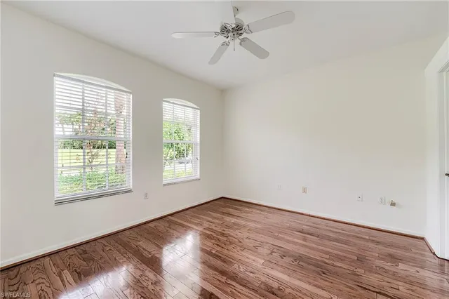 an empty room with wooden floor ceiling fan and windows