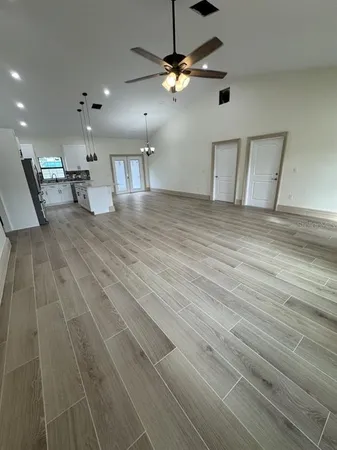 a view of an empty room with kitchen and chandelier fan