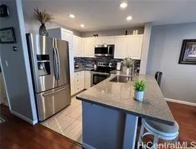 a kitchen with stainless steel appliances granite countertop a refrigerator a stove a sink a microwave a refrigerator and white cabinets with wooden floor