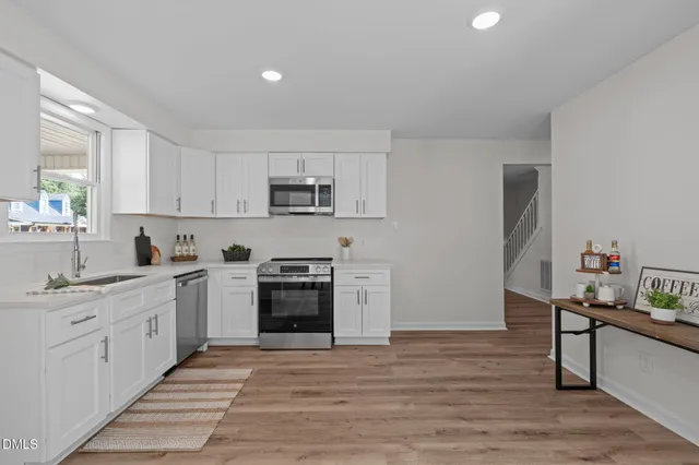 a kitchen with stainless steel appliances a sink dishwasher a stove top oven a refrigerator with white cabinets and wooden floor