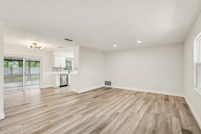 a view of empty room with wooden floor and kitchen view