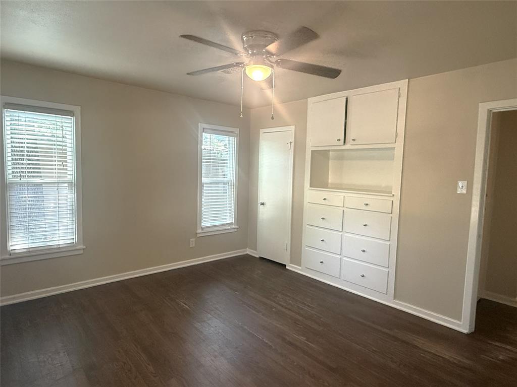 4718 Normandy Road Fort Worth, TX 76103 - Photo 8 of 26 Room featuring wood-finish flooring, two windows with blinds, a ceiling fan with integrated lighting, and built-in cabinetry with drawers and open shelving