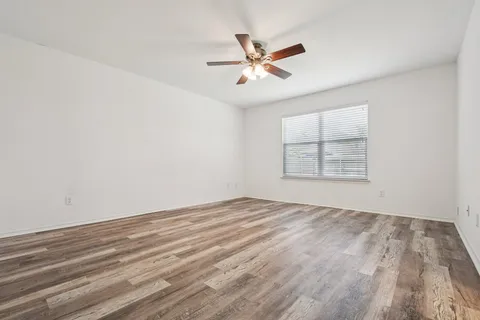 an empty room with wooden floor fan and windows