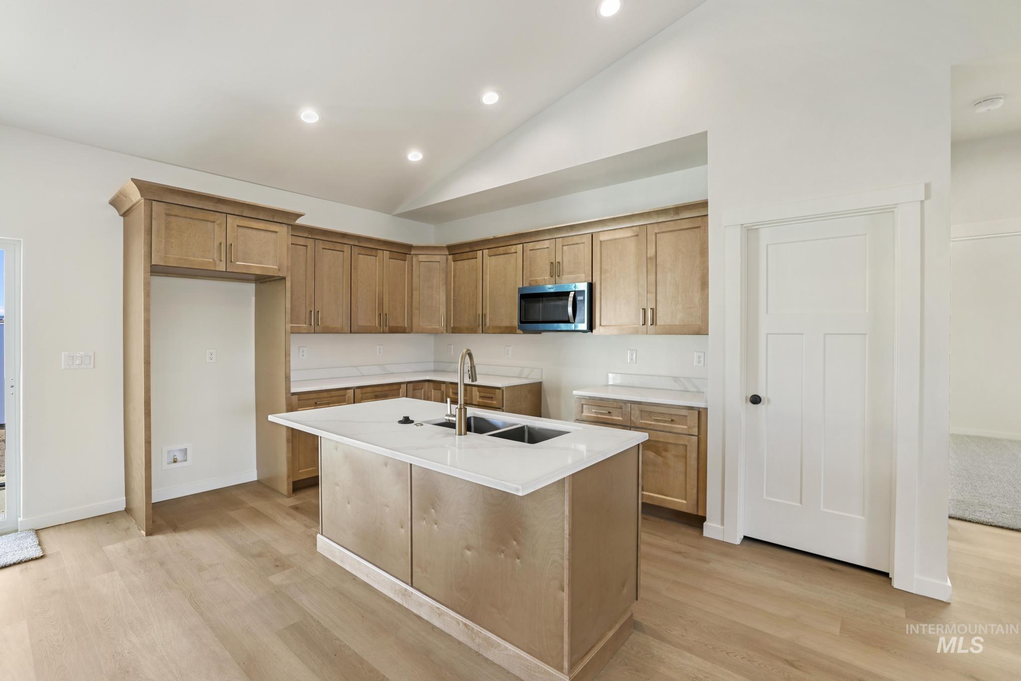 2014 Regan Street Jerome, ID 83338 - Photo 9 of 32 Kitchen featuring lofted ceiling, brown cabinetry, stainless steel microwave, a center island with sink, and light wood-style flooring