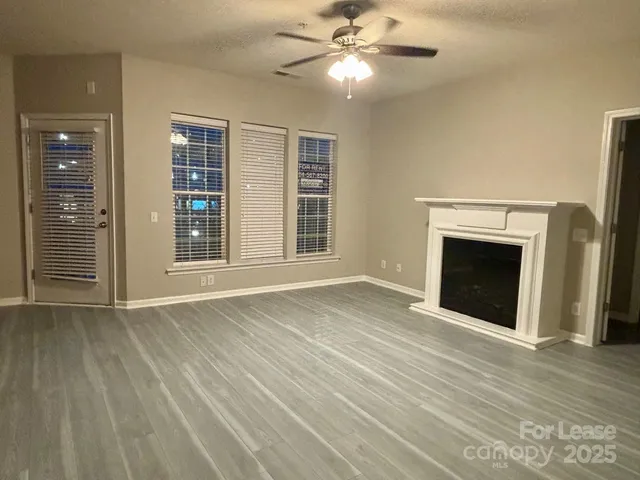 a view of an empty room with wooden floor fireplace and a window