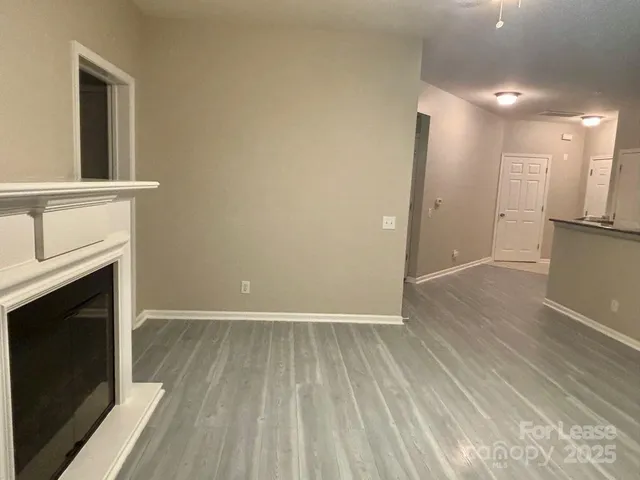 a view of an empty room with wooden floor and a kitchen
