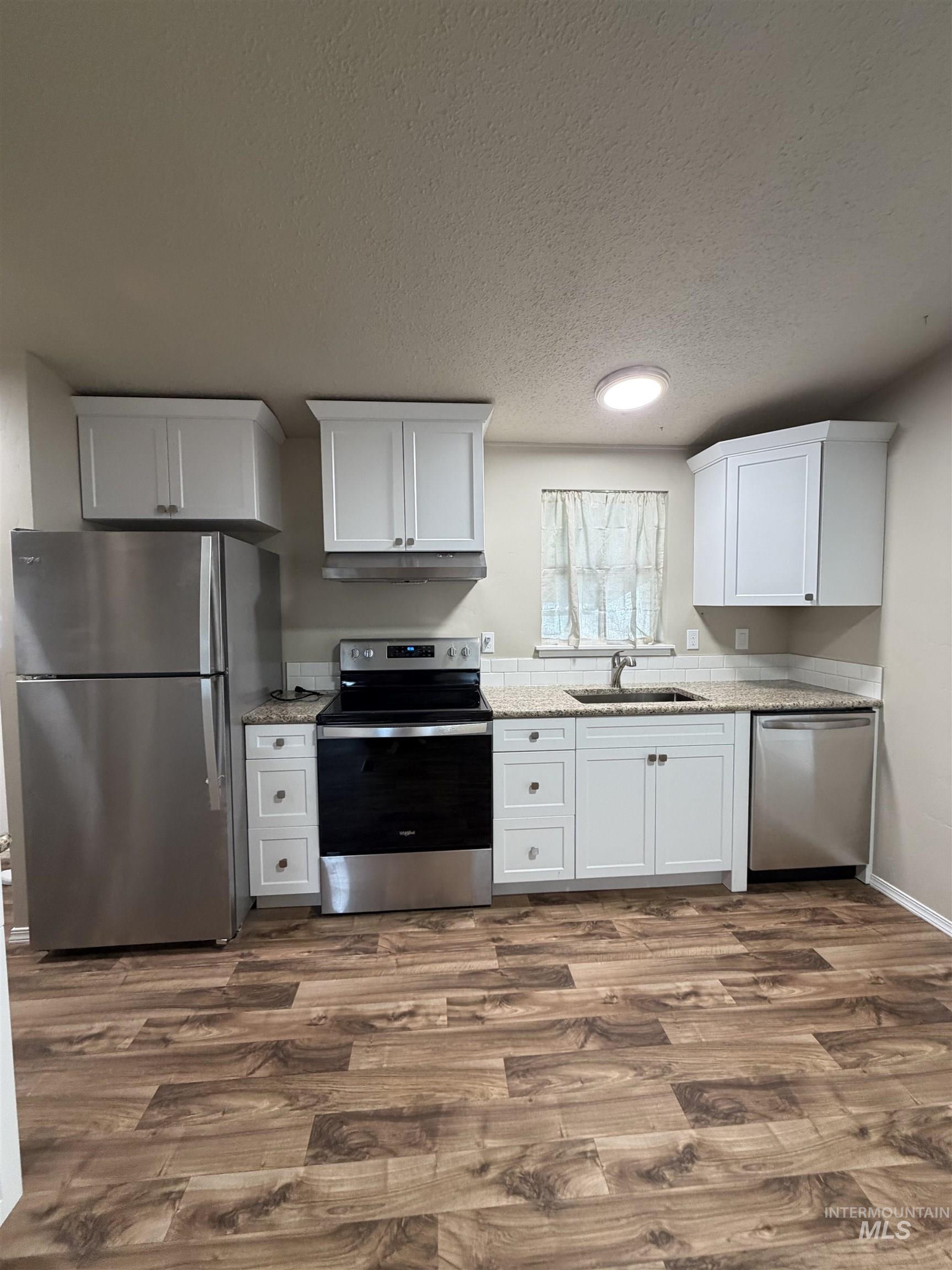 815 East Liberty Street Weiser, ID 83672 - Photo 5 of 25 Kitchen featuring stainless steel appliances, white cabinetry, light stone counters, dark wood-style flooring, and a textured ceiling