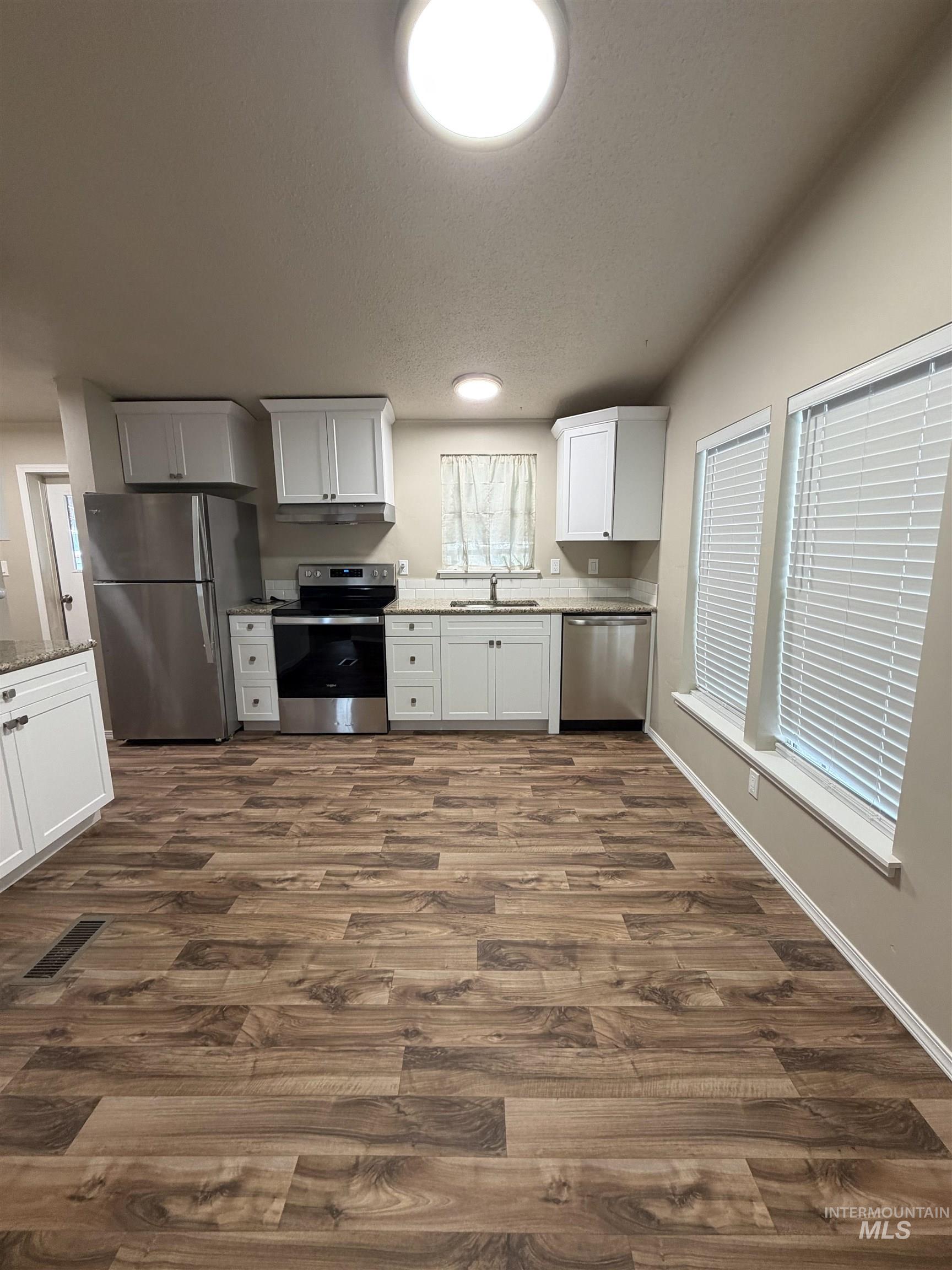 815 East Liberty Street Weiser, ID 83672 - Photo 7 of 25 Kitchen featuring stainless steel appliances, white cabinets, light stone countertops, dark wood-style floors, and a textured ceiling