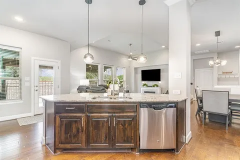 a kitchen with kitchen island granite countertop a stove a sink a dining table and chairs with wooden floor