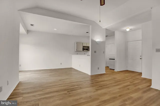 a view of an empty room with wooden floor and a kitchen