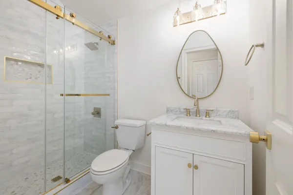 a bathroom with a toilet sink vanity granite and shower