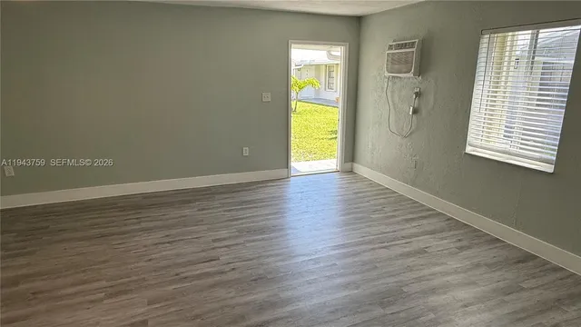 a view of an empty room with wooden floor and a window